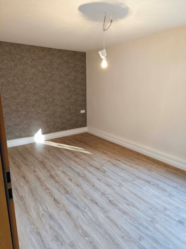 Ein fertiggestellter Raum mit neuem Vinylboden in Holzoptik und einer modern gemusterten Tapete. Das Licht fällt sanft durch ein Fenster. Der Raum sieht frisch renoviert aus.