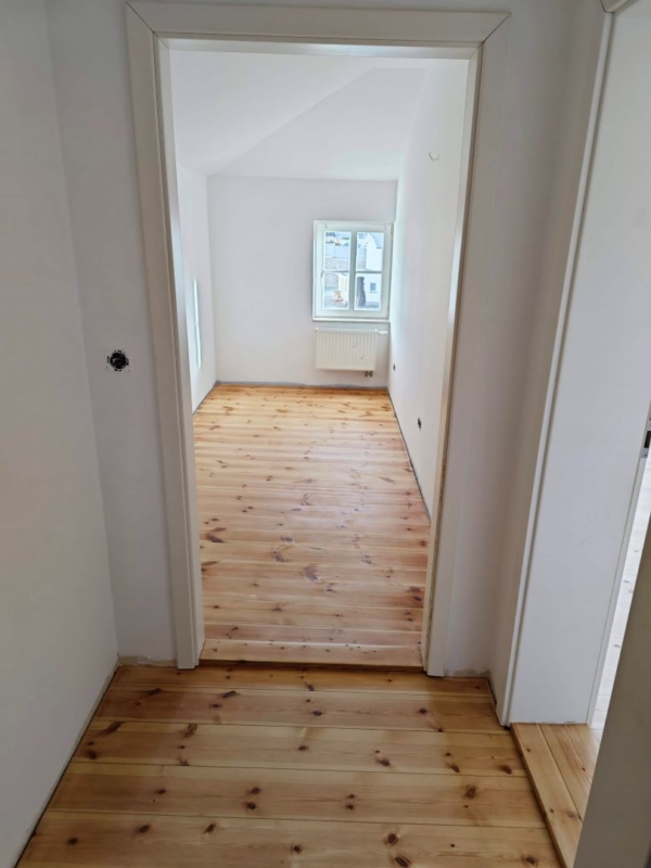Kleines Zimmer mit Holzboden, weißen Wänden und einem Fenster